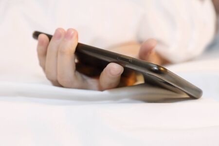 woman hold mobile phone in her hand while she sleep in bed