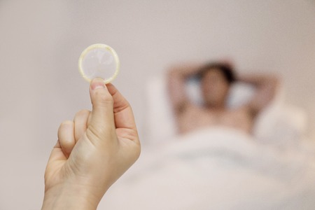 Woman holding condom with a man lying on bedの写真素材