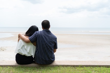 back view of young asian couple  sitting and huging each other with sea viewの写真素材