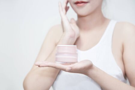 Asian woman hold a moisturizer cream in her hand and applying the cream on her faceの写真素材