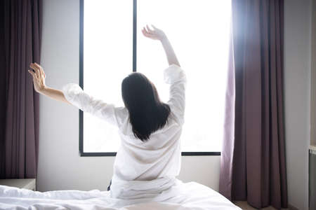 Back View of  Asian Woman Raise Her Hand Stretching in the Morning on Her Bedの写真素材