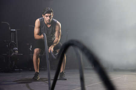 Caucasian Man Using Battle Ropes For Whipping Exercise  in a Gymの写真素材