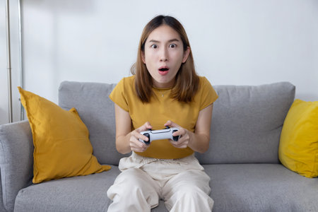 Excited Asian Woman Play Console Game with a Game Controller on Sofaの写真素材