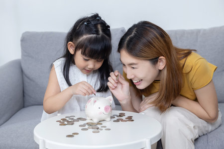 Asian Mother Help Her Daughter Put Coins Money into Piggy Bankの写真素材