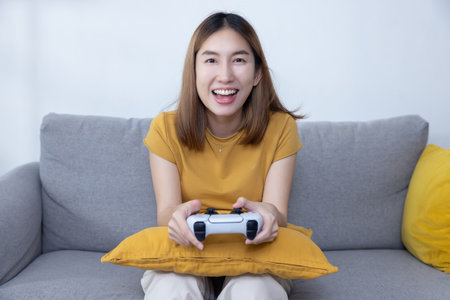 Happy Asian Woman Play Console Game with a Game Controller on Sofa