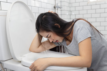 Side View of Asian Woman Vomiting into Toilet Bowlの写真素材