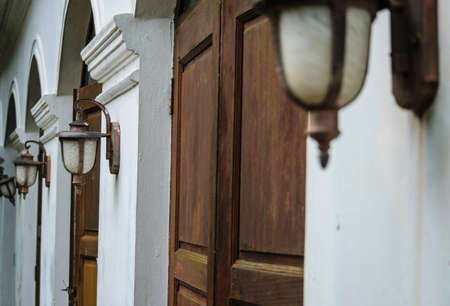 Ancient wooden door in old temple wall with lamp. Thailandの写真素材