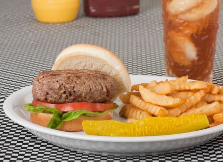 Hamburger on a bun with tomato and lettuce along with french fries, pickle and a drinkの写真素材