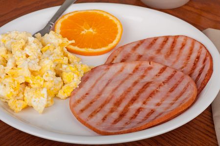 Plate of grilled ham and scrambled eggs with an orange sliceの写真素材