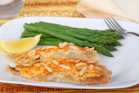 Fish fillets topped with crab meat sauce and almond slivers with asparagus and slice of lemonの写真素材