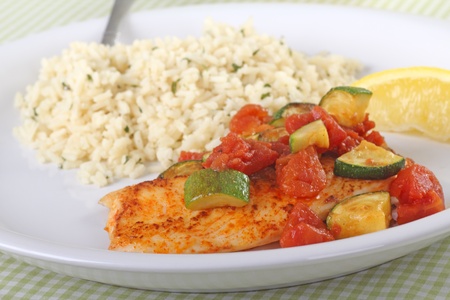 Fish fillet meal topped with tomato and zucchini with rice and a lemon sliceの写真素材