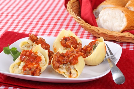 Stuffed pasta shells with tomato sauce and bread in the backgroundの写真素材