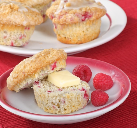 Buttered raspberry muffin on a plate with raspberry fruit