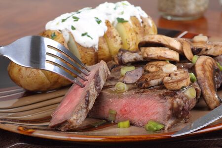 Steak covered with mushrooms and a baked potato with sour creamの写真素材