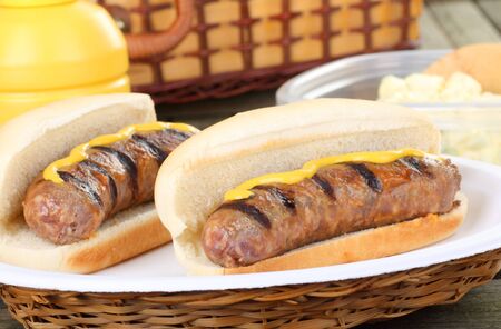 Two grilled bratwurst on buns with mustard on a picnic tableの写真素材