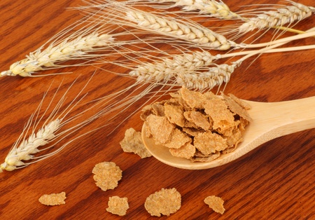 Wheat flakes on a spoon with wheat heads on a table
