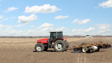 Red farm tractor with a plow in a farm field