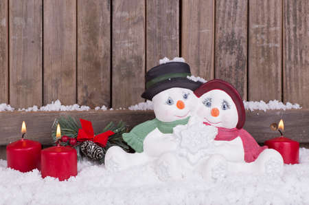 Christmas snowman figurine sitting in the snow with burning candlesの写真素材