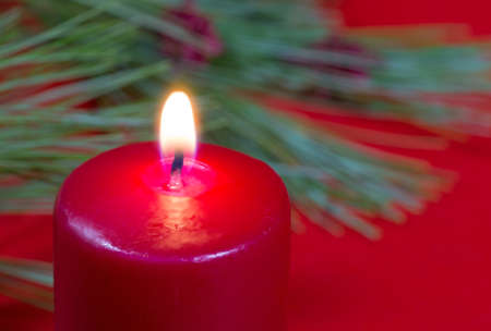 Closeup of a burning red candle with pine needles and red backgroundの写真素材