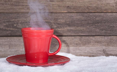 Red steaming cup of coffee on snow with wooden backgroundの写真素材
