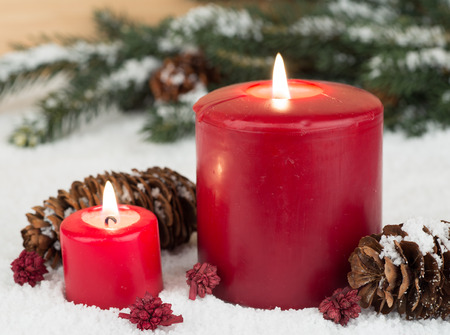Two red holiday candles with pine cones on snowの写真素材