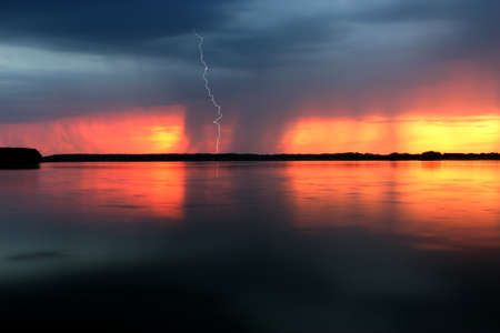 Thunderstorm at sunset with lightning bolt reflected in a lakeの写真素材