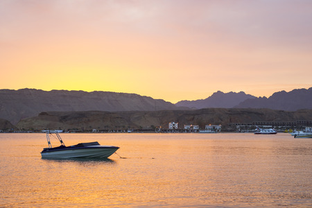 SHARM EL SHEIKH, EGYPT - MARCH 1, 2014: Motor boat is anchored among the Bay, evening sunset, red...