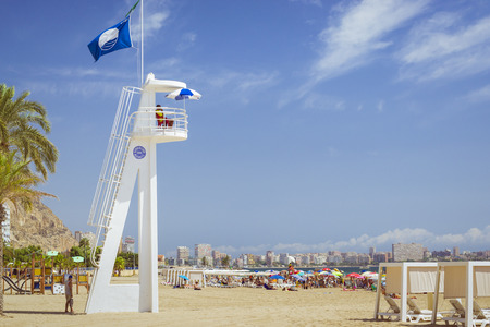 ALICANTE, SPAIN - SEPTEMBER 9, 2014: Sunny beach Playa del Postiguet near the castle Santa Barbara. Lifeguard on the tower. Tourists relax under umbrellas on the warm sand. Alicante, Valencian Community, Spainのeditorial素材