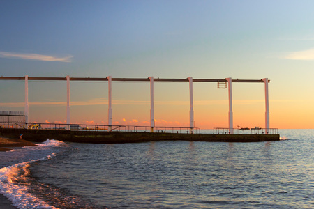 Concrete pier with a transport rail at top on seafront sinking into waves. Sunset on beach on Black sea in October. Sochi, Krasnodarskiy kray, Russiaの写真素材