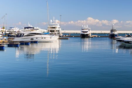 Luxury yachts and private boats moored at pier in Sochi seaport. In background is concrete promenade...