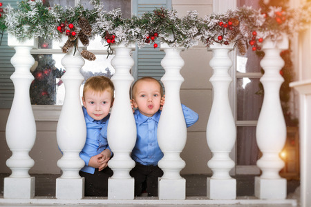 Two cute boy kid playing on porch, decorated in Christmas style. Waiting for New year in festive interior with garland of snow-covered pinesの写真素材