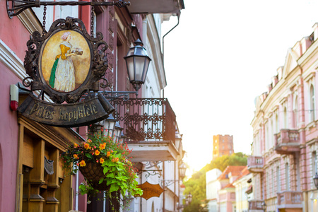 Vilnius, Lithuania - August 7, 2012: Forged signboard with image of woman with tea tray over entrance to cafe. Baltic architecture of central street of old city, view of mountain and Gedimin's Towerのeditorial素材