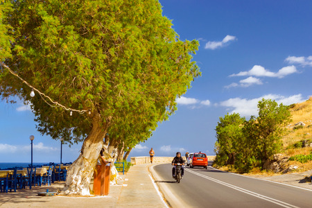 Rethymno, Greece - May 3, 2016: Athletic young girl running on the sidewalk about a car and a motorcycle going down the highway along promenade Emmanouil Kefalogianni. Crete islandのeditorial素材