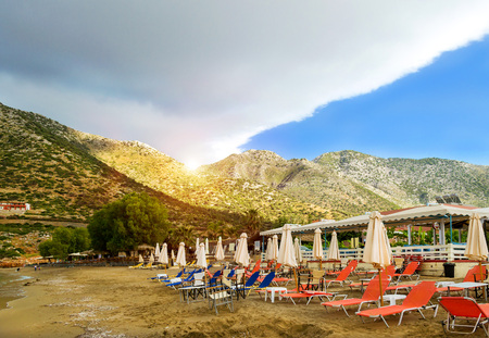 Sunny sandy Livadi beach in sea bay of resort village Bali in may. Views of mountain, shore, washed by waves and sun loungers with parasols where sunbathing tourists. Bali, Rethymno, Crete, Greeceのeditorial素材