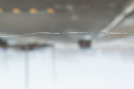 Broken car glass with crack on windshield of auto. Blurred grey backdrop of transport road in backgroundの写真素材