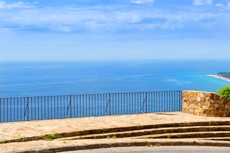 Panorama of sunny beach coast from height of stone observation deck with wrought iron railing. Spanish beach resort Blanes in summertime. View from Mirador De Sant Joan. Costa Brava, Catalonia, Spainの写真素材