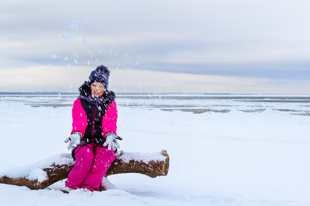 Winter day on snowy shore of Narva Bay. Snow on ice of frozen Finnish gulf. Narva-Joesuu resort town in Estonia. Severe Northern winter and snowy weather. Teenage girl walking on shore of ice seaの写真素材