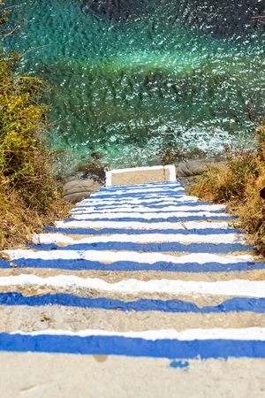 Concrete stairs down to ocean. Steps painted in colors of Greek flag, go down to sea waves. Varkotopos beach in sea bay of resort village Bali. Sheer cliff washed by waves. Crete, Greeceの写真素材