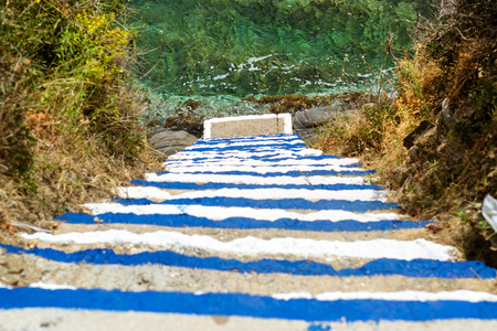 Concrete stairs down to ocean. Steps painted in colors of Greek flag, go down to sea waves. Varkotopos beach in sea bay of resort village Bali. Sheer cliff washed by waves. Crete, Greeceの写真素材