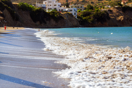 Surf and tide of foamy waves on a sandy beach. Sunny sandy Livadi beach in sea Bay of resort village Bali. Sea waves wash the sandy deserted beach. Bali, Rethymno, Crete, Greeceの写真素材