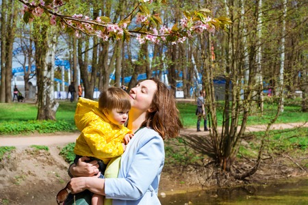 Young woman with a child in her arms happy Sakura blossom in spring Park. Joy of motherhood and child development. Cherry blossom tree in late spring. Flora of North-West of Russia, Saint-Petersburgの写真素材