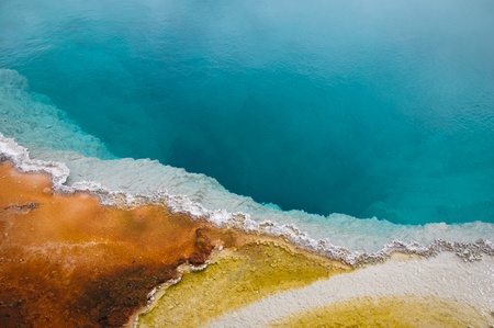 Stock Photo: Black pool, one of many geothermal feature at Yellowstone National Park with a deep rich blue color & white, orange & yellow algae around its edge の写真素材