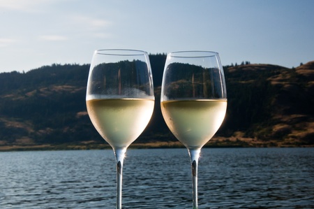 Closeup of two glasses of white wine with condensation on the outside of them next to a lakeの写真素材