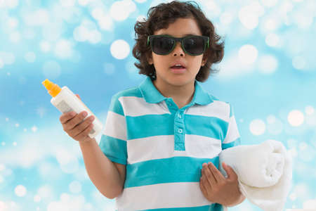 Schoolchild boy ready to go to the beach . Boy holding  sun tan lotion bottle. and rolled towelの写真素材