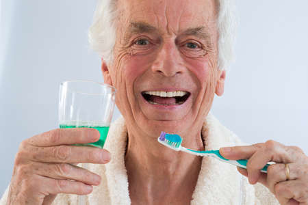 thooth care- senior man holding teeth brush and mouthwash in a glass
