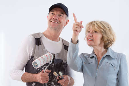 Senior woman showing to a painter man where to paint on the wall isolated on white backgroundの写真素材