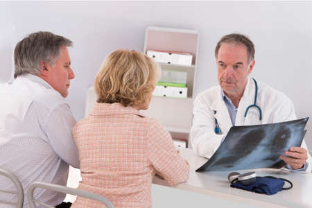 Doctor showing diagnosis of x-ray image to senior patient sitting at office deskの写真素材