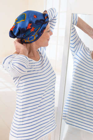 Senior woman looking at mirror and putting her scarfの写真素材