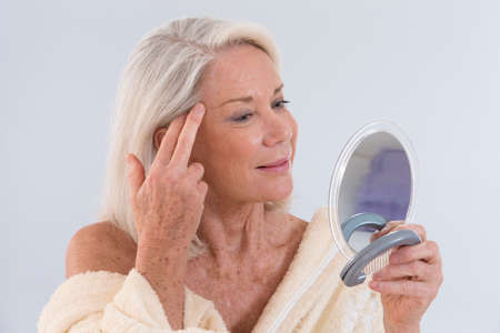 Mature woman looking at herself in the mirror showing her wrinklesの写真素材