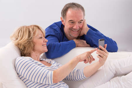Happy mature couple using smartphone together at home in living roomの写真素材